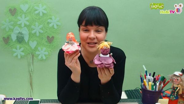 Çiçek Bebekler video karesi: eğitmen pembe ve mor etekli iki küçük çiçek bebeği gösteriyor