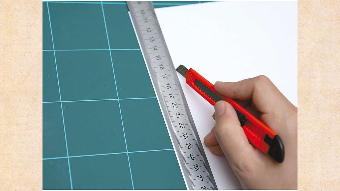 Kesim matı üzerinde cetvel ve maket bıçağıyla desenli kağıttan eşit şeritler kesiliyor