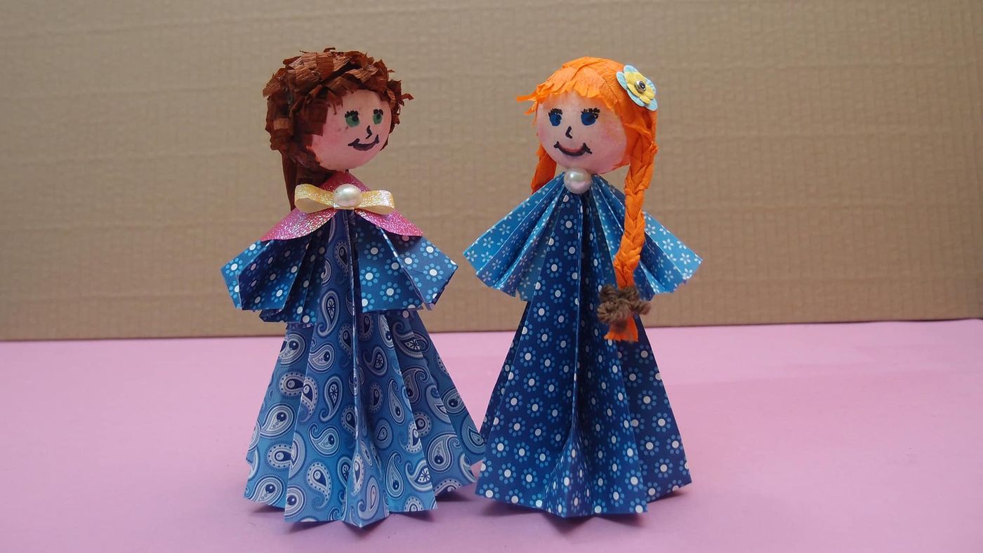 Origami Çocuklar ikilisi hafif açıdan, farklı desenli mavi elbiseler ve yaka süsleri görünüyor