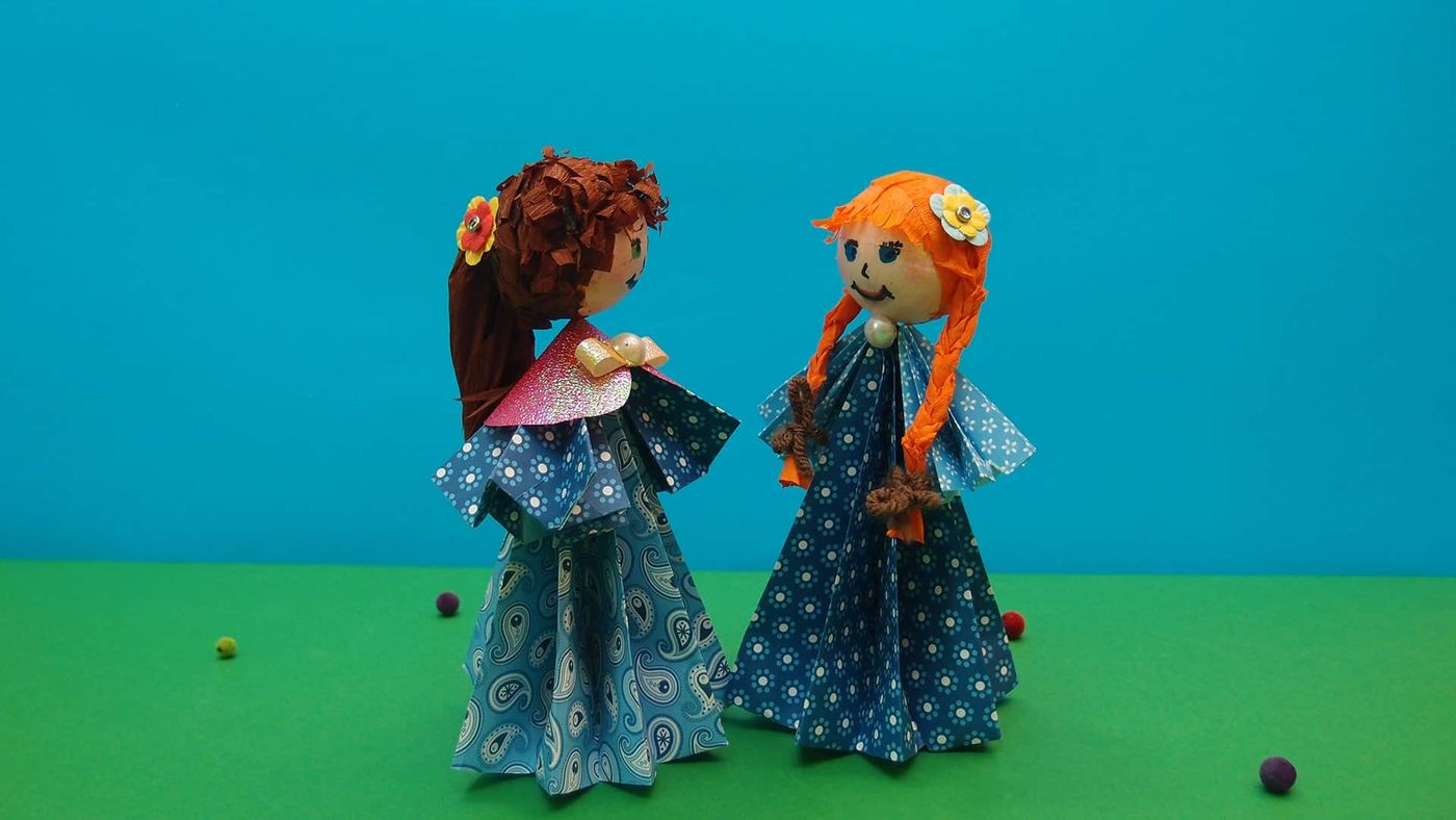 İki origami bebek birbirine dönük yandan duruyor, saçlardaki çiçek tokalar belirgin