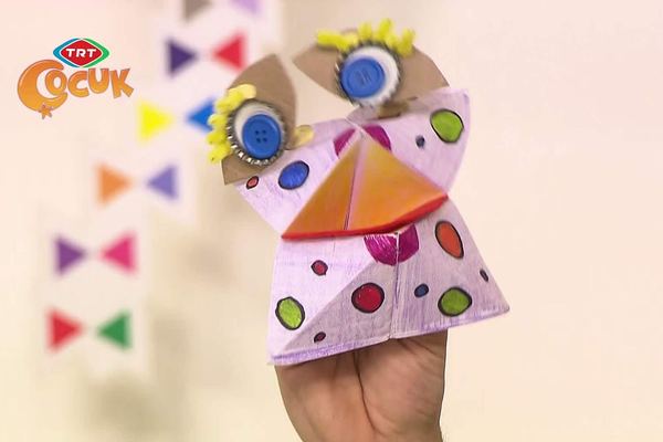 Tuzluk kukla elde açılmış: pembe benekli katlanmış kağıt, düğme gözler ve turuncu üçgen ağız
