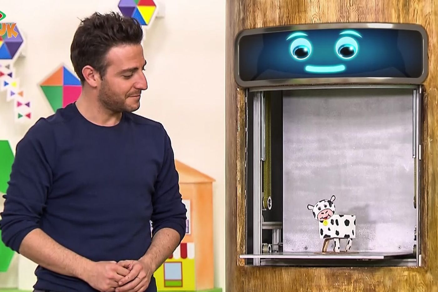 Programdan kare: sunucu stüdyoda, yanındaki bölmede siyah benekli karton inek duruyor