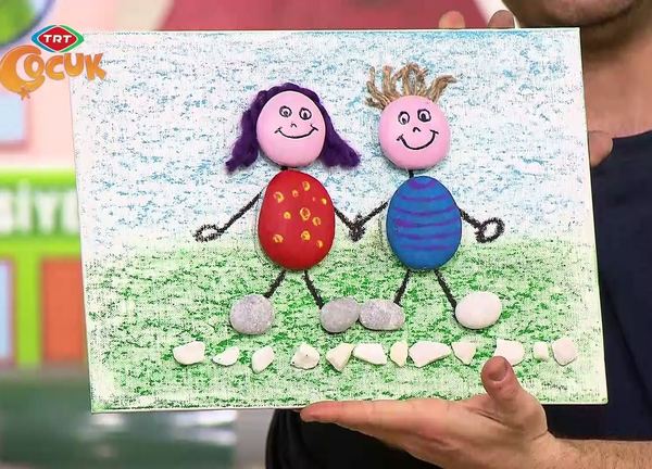 Taş boyama tablosu: boyalı taşlardan el ele tutuşan iki çocuk figürü, pastel boyalı çimen zeminde