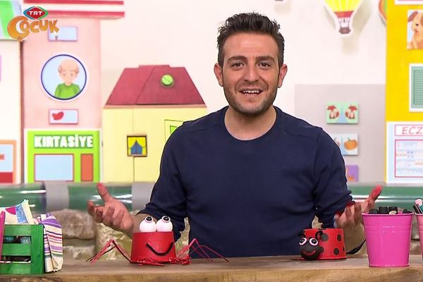 Yengeç etkinliği program karesi: sunucu masadaki kırmızı bardaktan yengeç ve uğur böceğini tanıtıyor