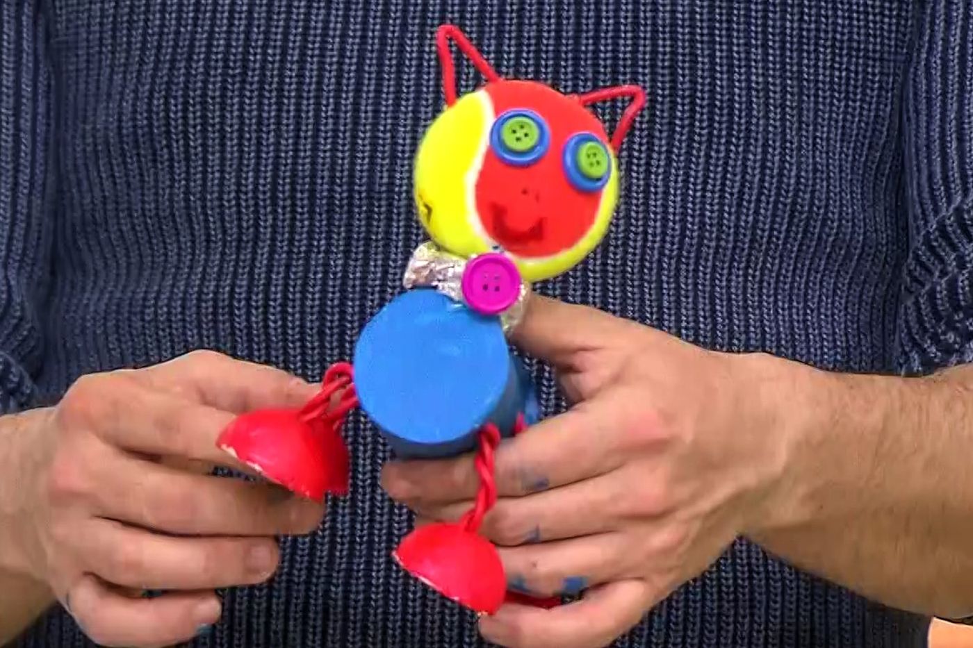 Elde tutulan kırmızı-sarı kafalı, düğme gözlü, mavi gövdeli ve kırmızı bacaklı küçük robot