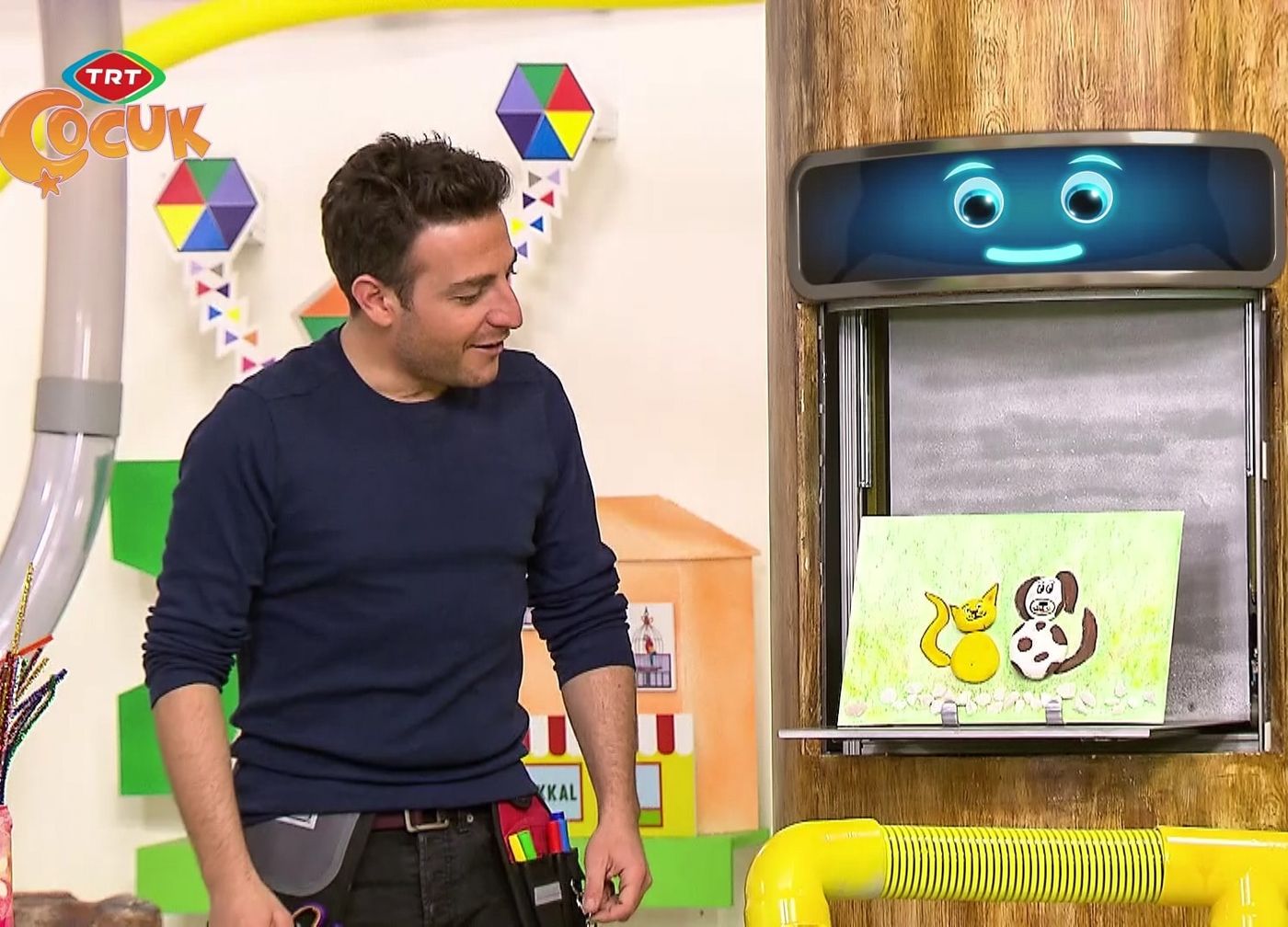 Programdan kare: sunucu stüdyoda, kedi ve köpek taş tablosu dekordaki bölmede duruyor