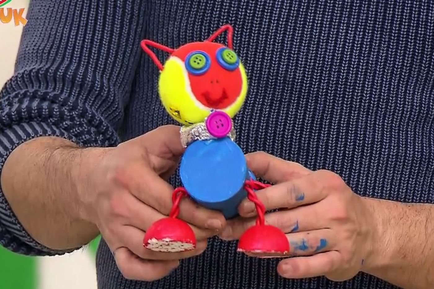 Kedi kulaklı kırmızı-sarı kafası ve mavi kapak gövdesiyle küçük robotun önden yakın görünümü