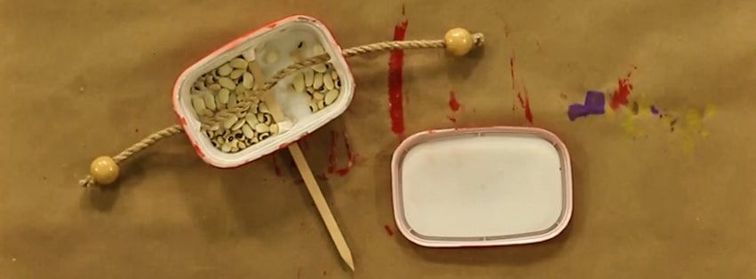İçine tohum konmuş plastik kutu, uçları boncuklu ip ve tahta çubuk, yanında kutunun kapağı