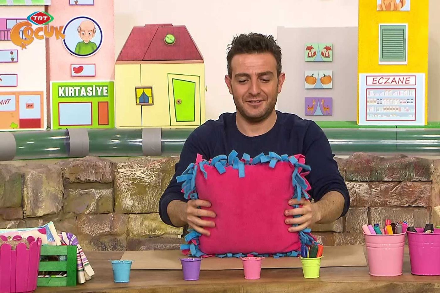 Sunucu masada mavi saçaklarla çevrili pembe polar yastığı iki eliyle tutuyor