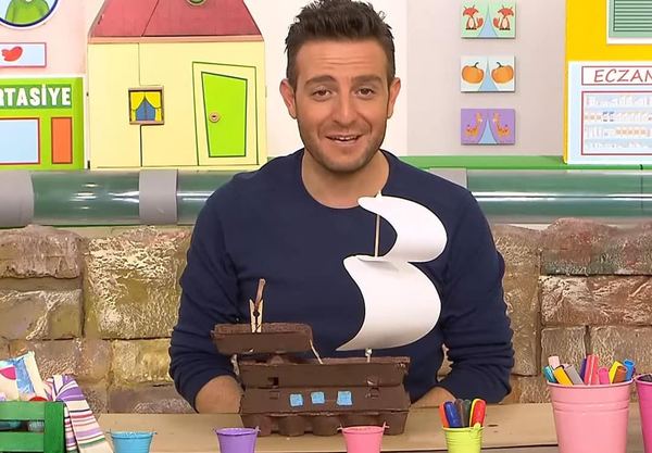 Korsan gemisi yapılan programdan kare: sunucu masadaki yumurta kolisinden beyaz yelkenli gemiyi gösteriyor