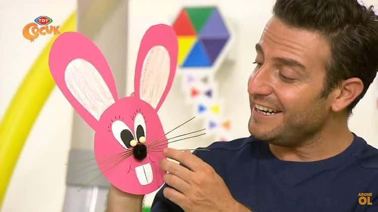 Sunucu pembe kağıttan uzun kulaklı, bıyıklı tavşan el kuklasını gösteriyor