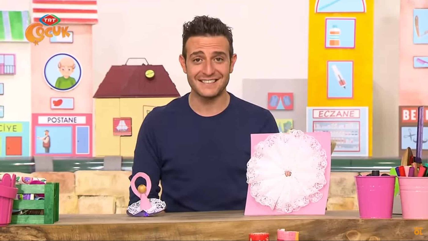Stüdyoda masada balerin fırıldak ve dantel kağıt yelpazeli pembe panoyla gülümseyen sunucu