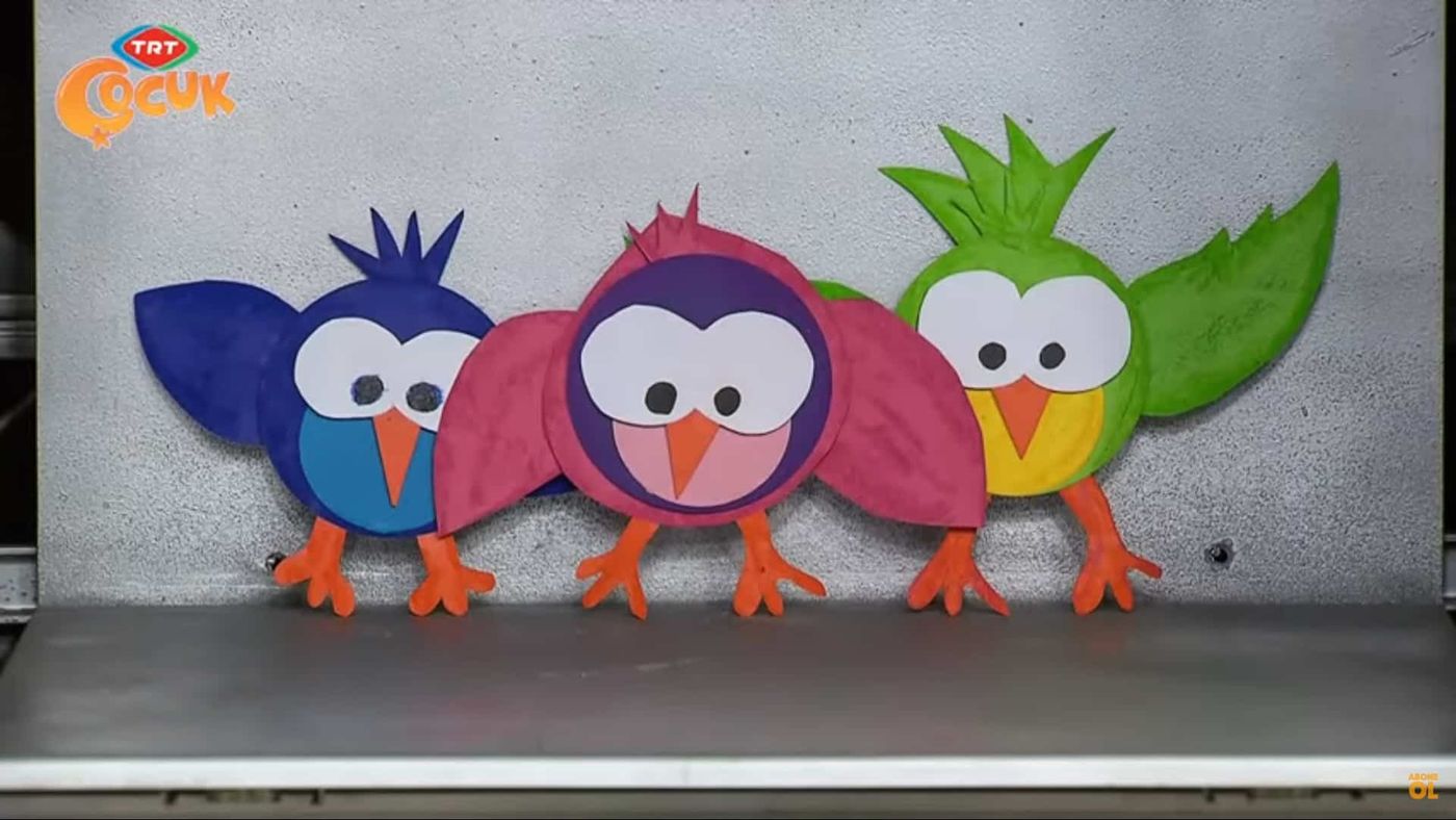 Mavi, pembe ve yeşil kağıttan üç kuş, turuncu gaga ve bacaklarıyla yan yana