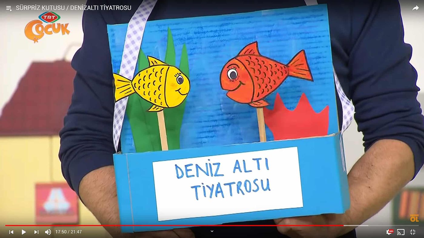 Omuzdan asılan karton tiyatro kutusunda çubuğa takılı sarı ve kırmızı kağıt balıklar, yakın çekim