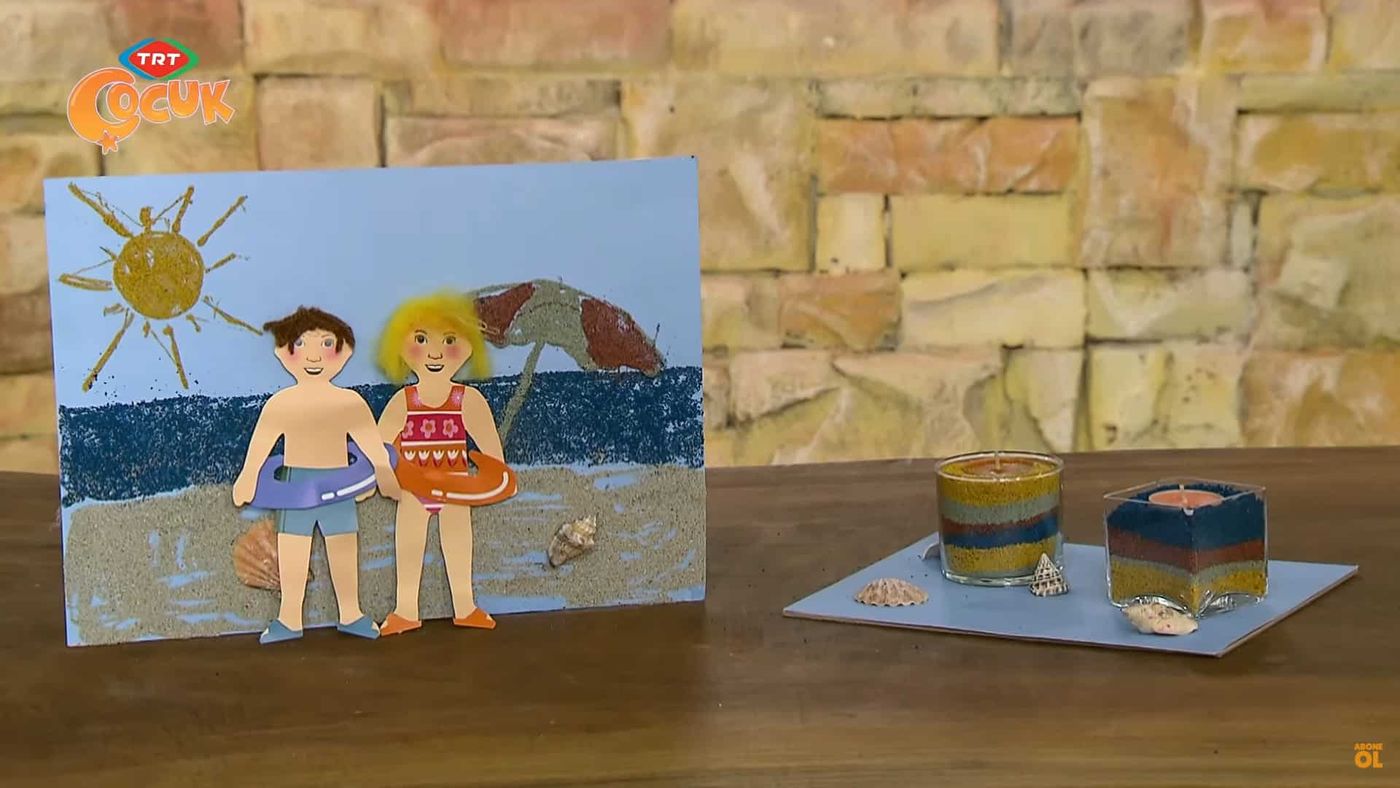 Kum boyama plaj tablosu ve renkli kum katmanlı cam kaplar masada birlikte duruyor