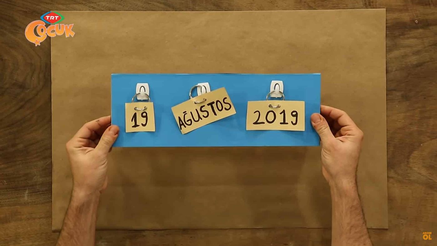 Mavi kartona yapışkan askılar ve halkalarla takılmış 19, Ağustos, 2019 kartları; iki elle gösteriliyor