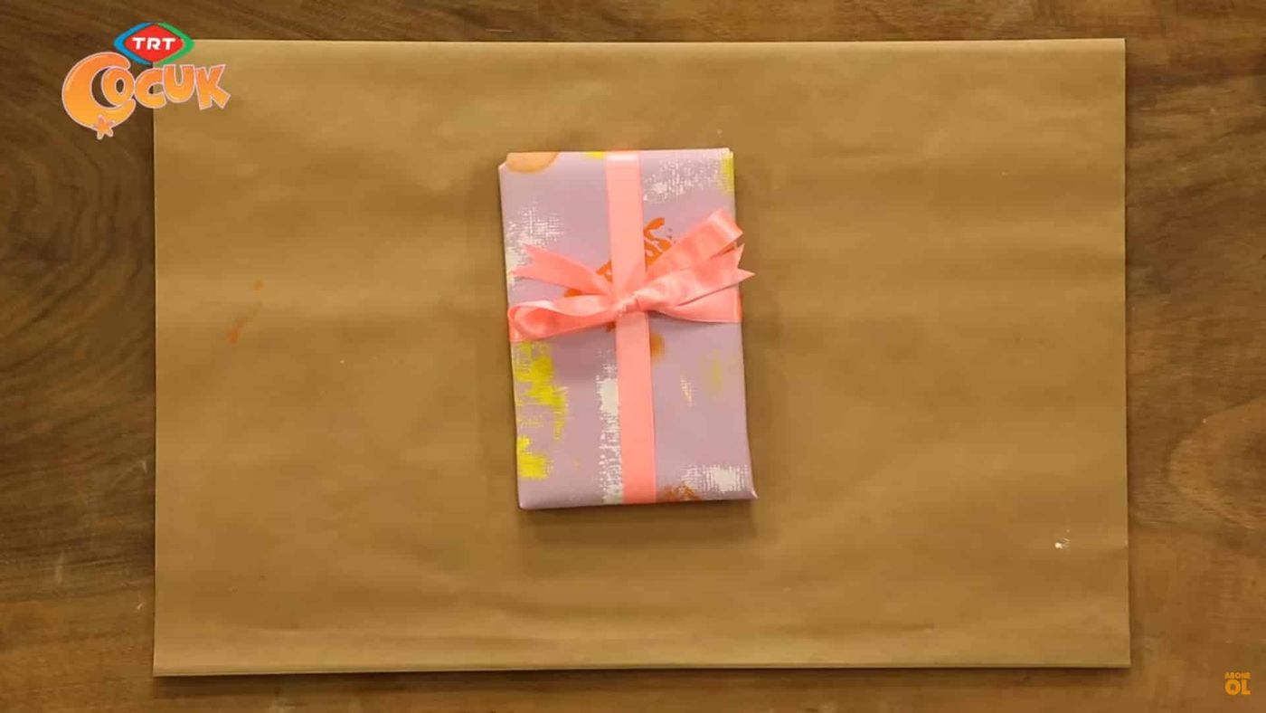 Kraft kağıt üzerinde baskı desenli leylak kağıtla sarılmış, pembe kurdeleli küçük paket