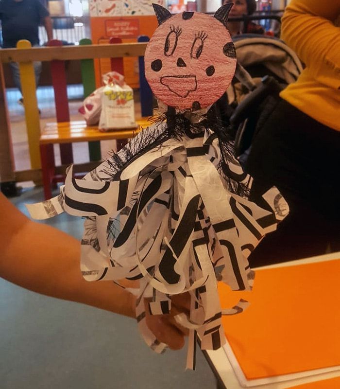 Pembe tonlarda boyanmış iskelet yüzlü kukla, kulakları ve desenli kağıt şerit eteğiyle atölyede