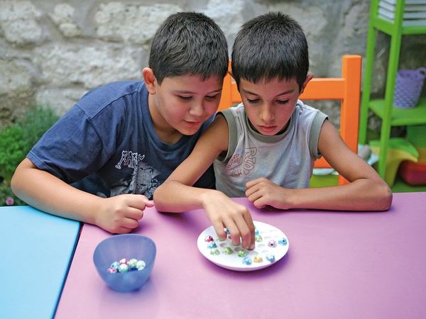 Masada iki çocuk bir tabaktaki renkli bilyelerle ev yapımı solo test oynuyor