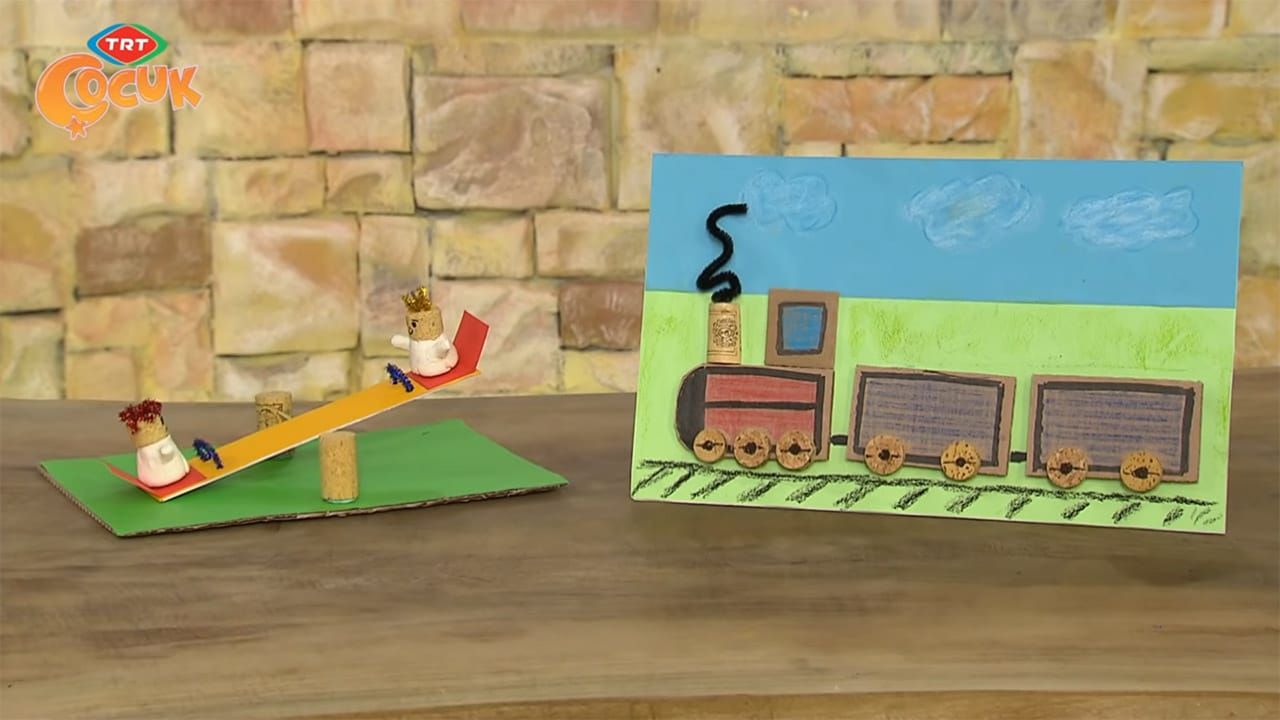 Yeşil karton üzerinde mantar tıpalı tahterevalli ve arkasında mantar tekerlekli tren tablosu