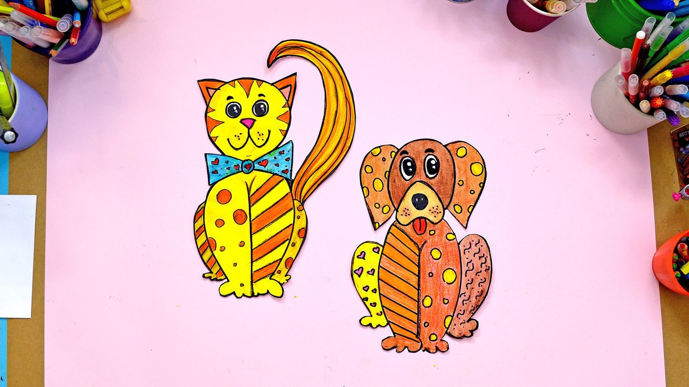 Dış hatlarından kesilmiş boyalı kedi ve köpek figürleri pembe masa üzerinde yan yana, kuklaya dönüşmeye hazır