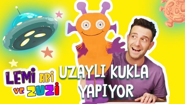 Kartondan uzaylı kukla videosunun kapağı: sunucu yanında turuncu uzaylı kukla ve uçan daire çizimi