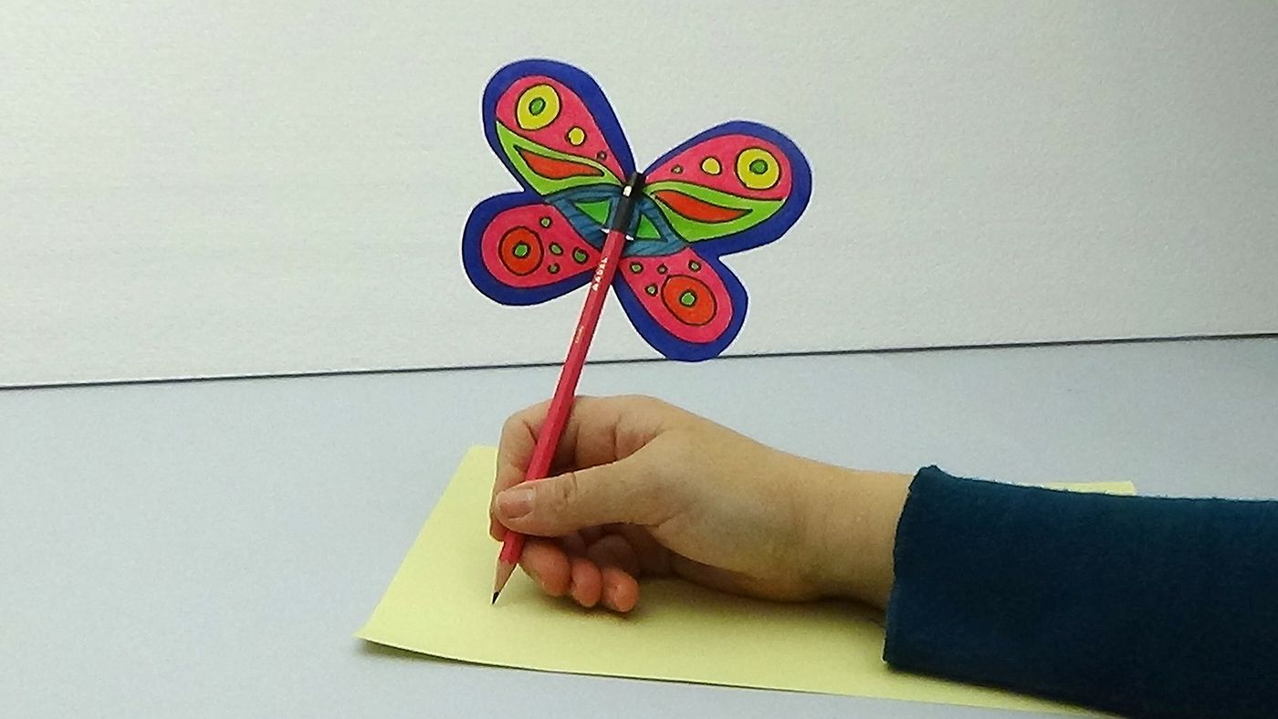 Pembe desenli kelebek kalem süsüyle sarı kağıt üzerinde yazı yazan bir el, kanatlar kalemin tepesinde