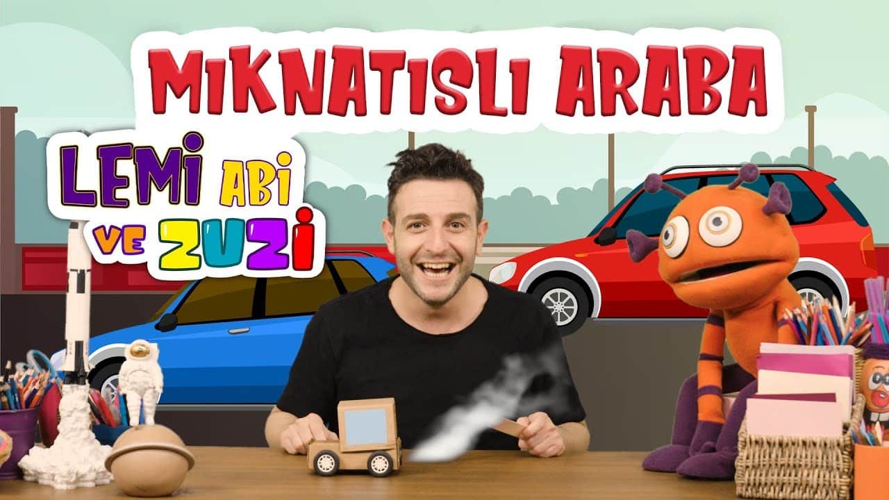Mıknatıslı araba video kapağı: sunucu ve turuncu kukla karakter masadaki kutu arabayı gösteriyor