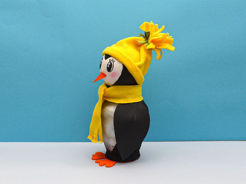 Sarı püsküllü bere ve atkı takmış kavanoz penguenin yandan görünümü, turuncu gaga sola dönük