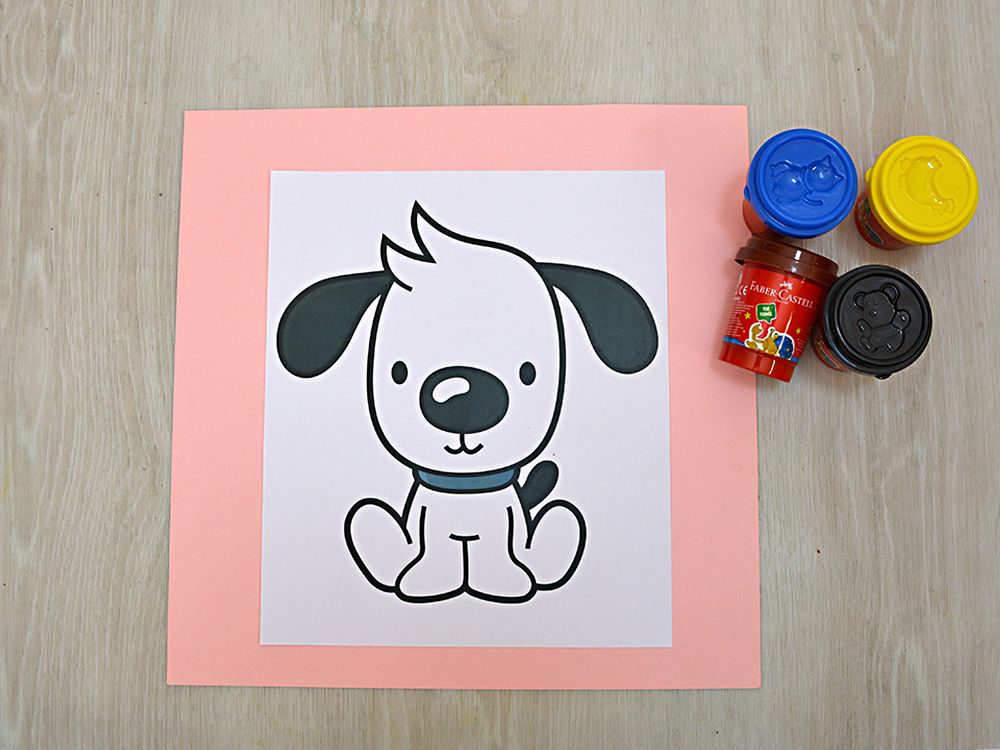 Pembe kartona yapıştırılmış oturan yavru köpek boyama sayfası ve renkli oyun hamuru kutuları